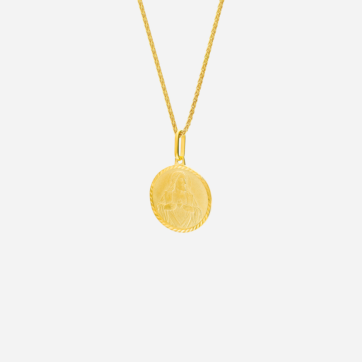 sacred heart pendant in 22k yellow gold with intricate engraving, hanging from a twisted gold chain.