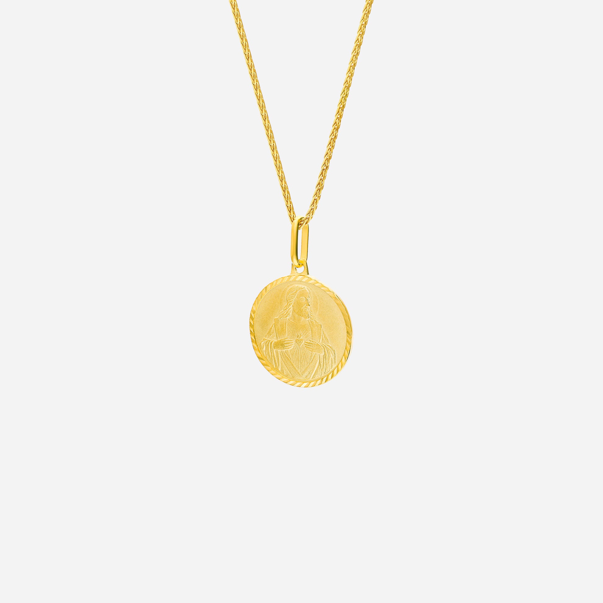 Sacred Heart pendant in 22K yellow gold with intricate engraving, hanging from a twisted gold chain.